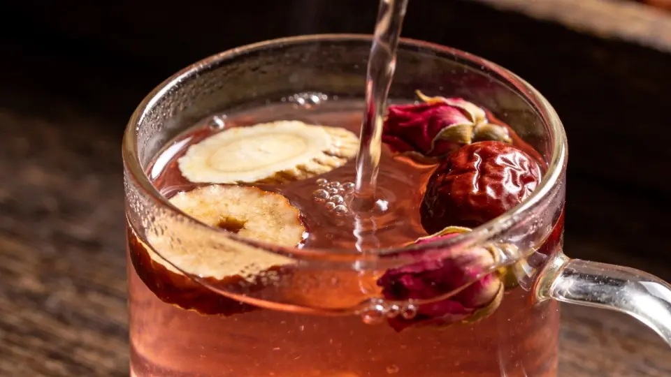 An close-up showcasing natural dried ginger slices, sweet red dates, and dark crimson Pingyin rose buds steeping elegantly in a clean glass teacup An close-up showcasing natural dried ginger slices, sweet red dates, and dark crimson Pingyin rose buds steeping elegantly in a clean glass teacup